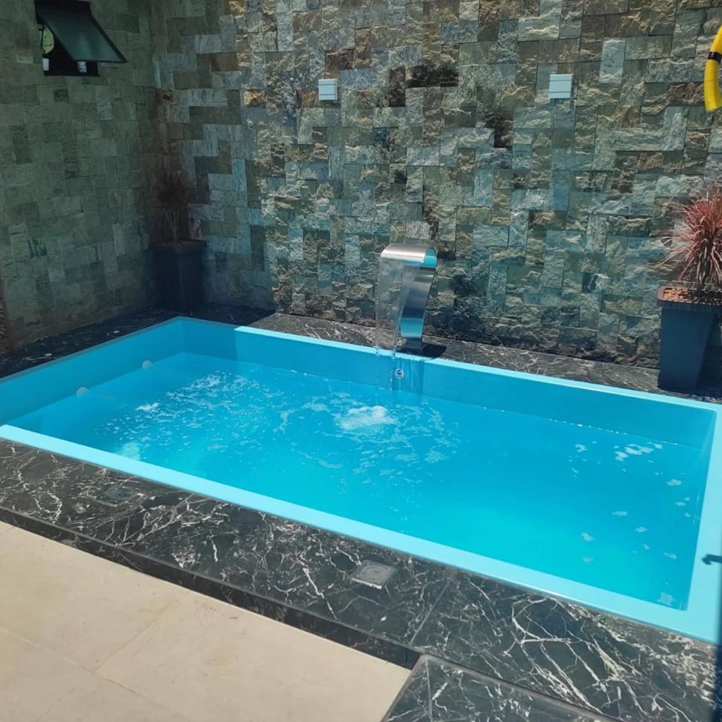 Piscina com cascata inox e parede de pedra natural